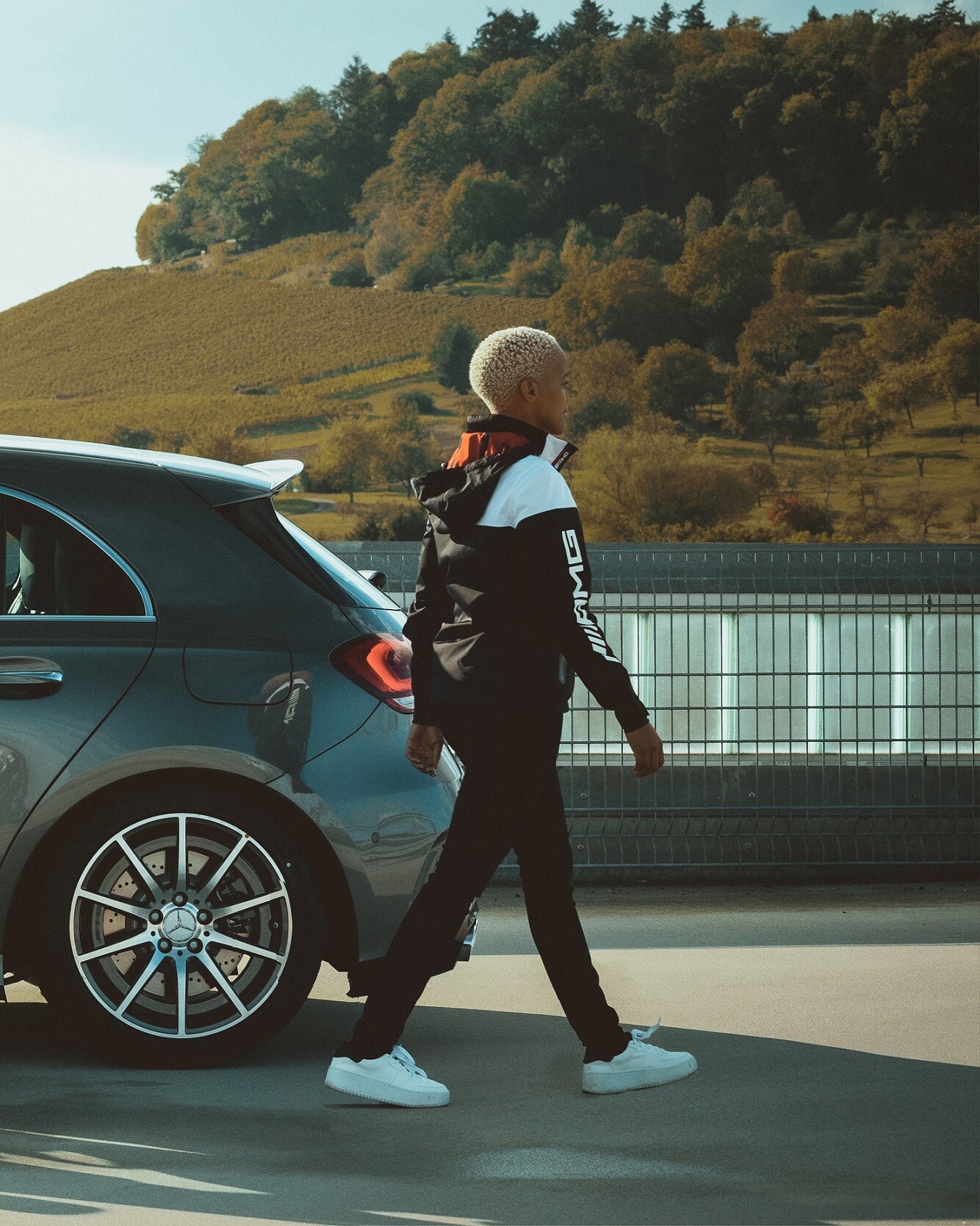 Mercedes-Benz AMG Collection | Mercedes-Benz A young woman in an outfit from the AMG Racing Collection walking next to her Mercedes.